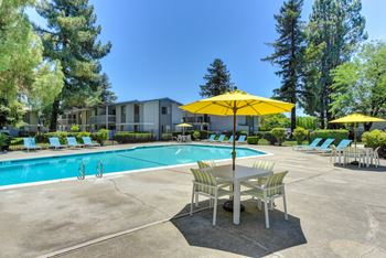 Swimming Pool with Lounge Seating and Tables. Tables have bright yellow umbrellas for shade. at Renaissance Park Apartments, Davis, CA